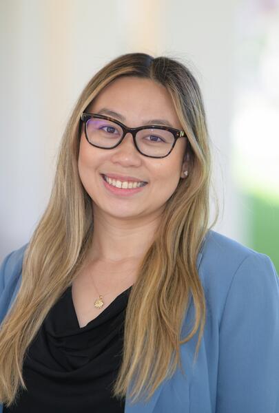 UCR staff member Amy Gu has long blonde hair and glasses. She wears a blue jacket, black shell top, and a gold necklace. 