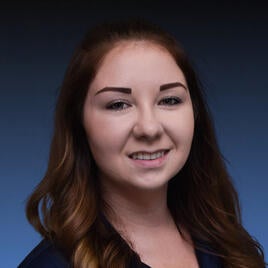 Head shot of UCR staffer Brittany Fraser. She has long, brown wavy hair that curls around her shoulders. Brittany has a smile on her face and wears a dark polo shirt.